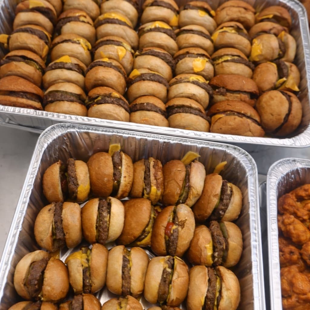 Black Angus cheeseburger sliders lined up in catering trays