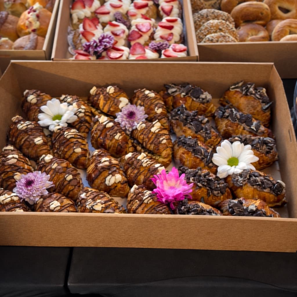 Boxes of croissants — chocolate-drizzled, almond, and danishes with edible flowers