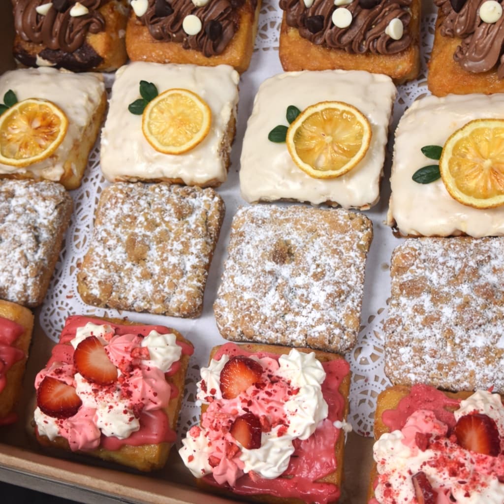 Box of gourmet pastries — chocolate-iced, lemon-glazed, powdered, and strawberry-cream squares